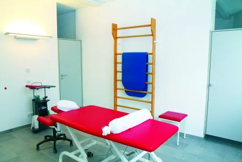 Heller Behandlungsraum mit roter Behandlungsliege und Sprossenwand
